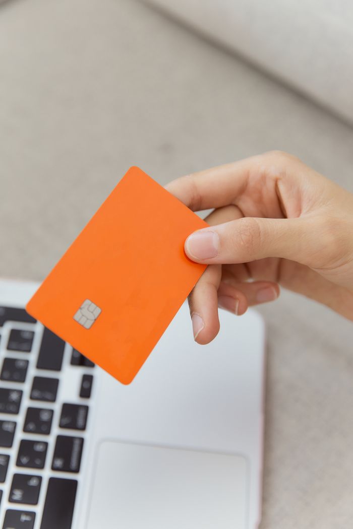 A close-up of an orange credit card held over a laptop, highlighting digital payment.
